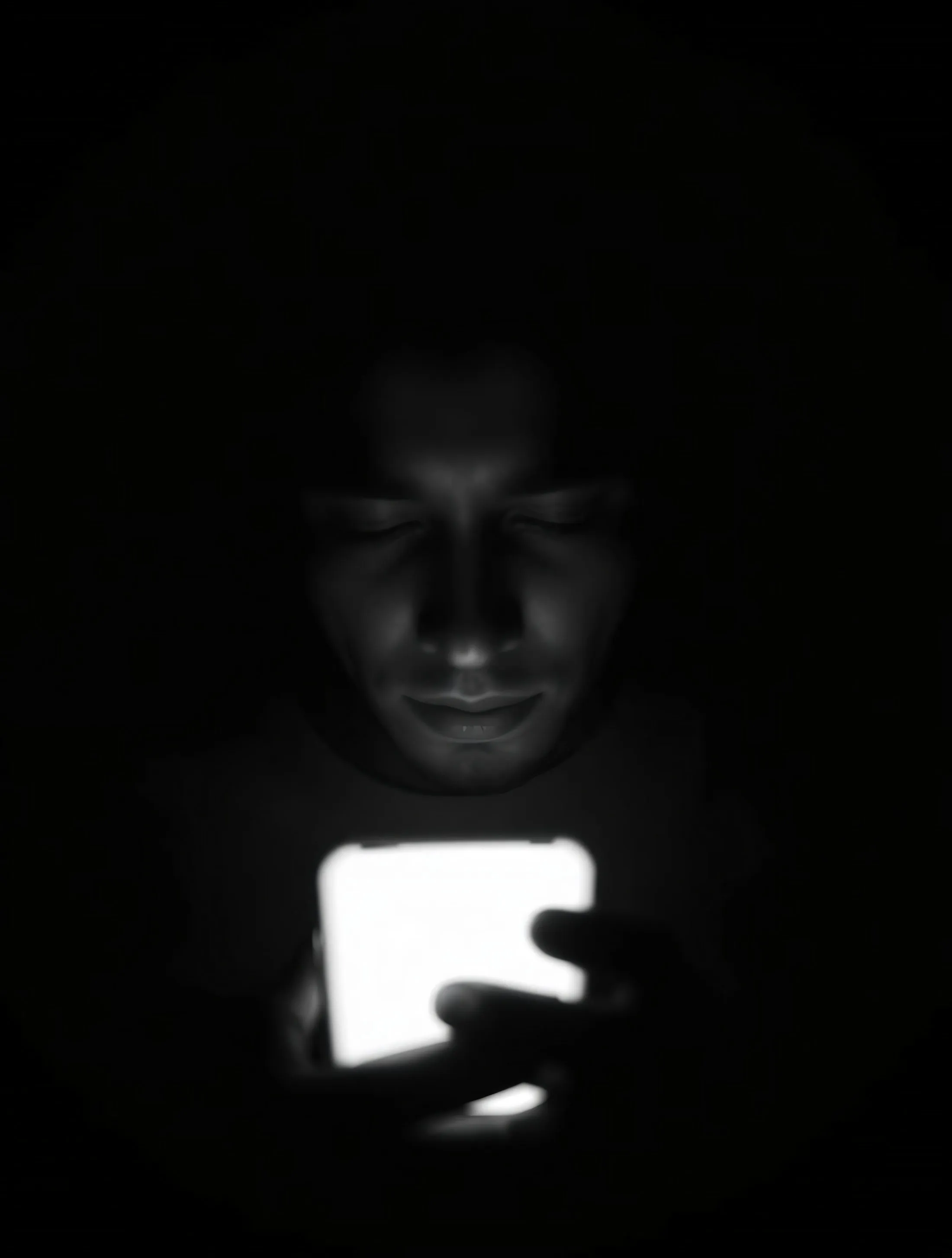 A person in the dark, face lit by a phone screen